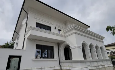 Bela kuća na sprat sa nizom lukova u prizemlju, okvirima oko prozora i vencem ispod krova