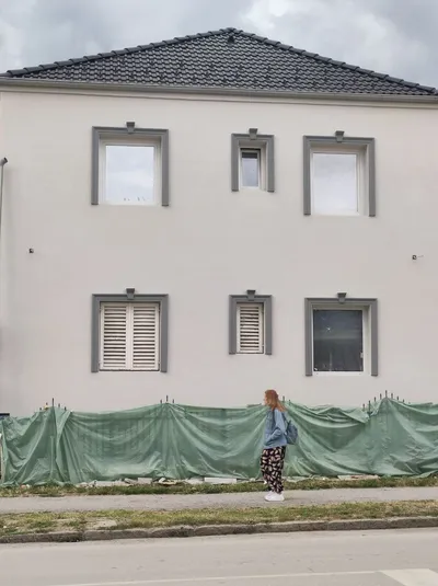 Bela kuća na dva sprata sa sivim okvirima i ključevima oko svih prozora, snimljena pred kraj radova