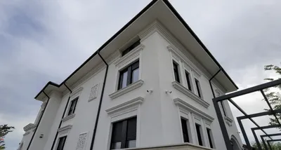 Bela kuća na tri nivoa sa okvirima oko svih prozora, vencem ispod krova i lajsnama između spratova