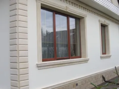 Bela fasada sa bež okvirima oko prozora, bež kockama na uglu i ukrasnim frizom ispod krova