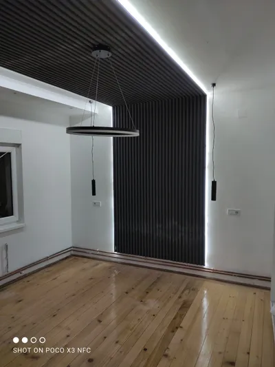 Soba sa crnim letvicama od poda preko plafona, LED trakom koja ih uokviruje, visećim lampama i lusterom prstenom