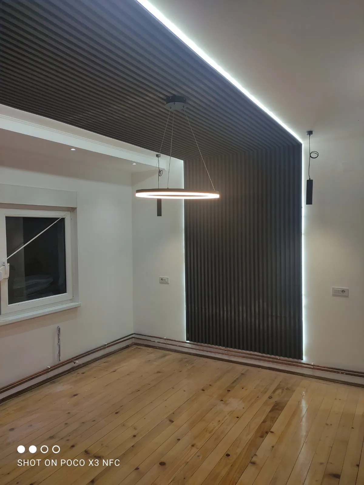 Crne letvice preko zida i plafona sa LED trakom Prazna soba sa crnim letvicama koje idu preko zida i plafona, LED trakom duž ivice i lusterom u obliku prstena
