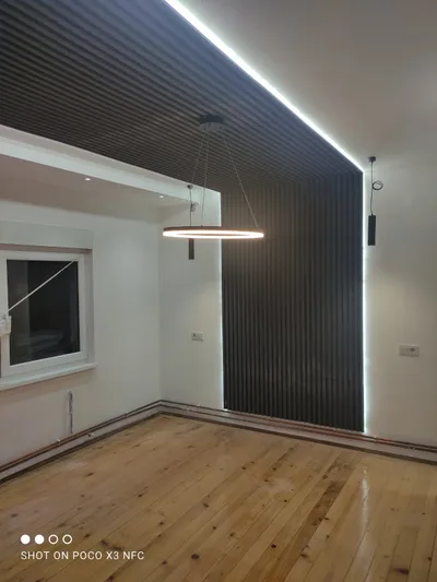 Prazna soba sa crnim letvicama koje idu preko zida i plafona, LED trakom duž ivice i lusterom u obliku prstena