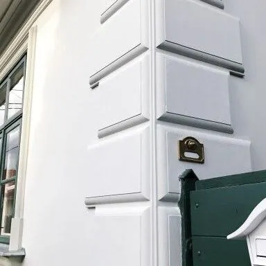 Velike fasadne kocke od stiropora na uglu bele kuće, naizmenično duže i kraće, pored zelene kapije