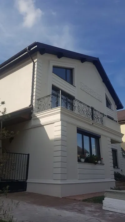 Kuća na sprat sa balkonom, horizontalnim kockama na uglu, okvirima oko prozora i vencem ispod balkona