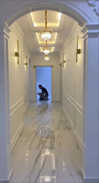 Dug hodnik sa lučnim prolazom, belim ram lajsnama na zidovima, kristalnim lusterima, zidnim lampama i mermernim podom