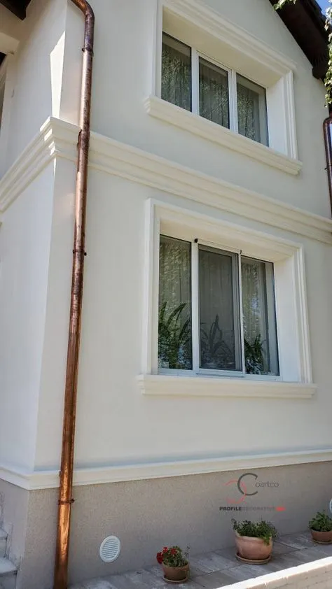Najlepše fasade na kućama: bela kuća sa kockama i vencem Bela fasada kuće sa ukrasnim okvirima oko prozora, ugaonim kockama i vencem između spratova