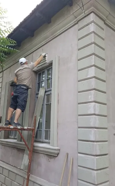 Majstor na skeli postavlja fasadnu lajsnu oko prozora, a pored su već postavljene kocke na uglu kuće