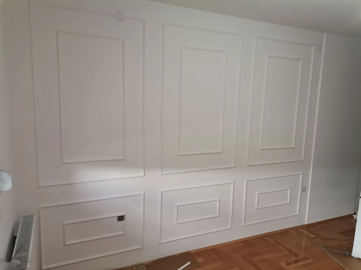 Ramovi na zidu: beli zid sa ram lajsnama od stiropora Beli zid ukrašen ramovima od stiropora: tri velika i tri mala polja iznad parketa, klasičan izgled kao gips