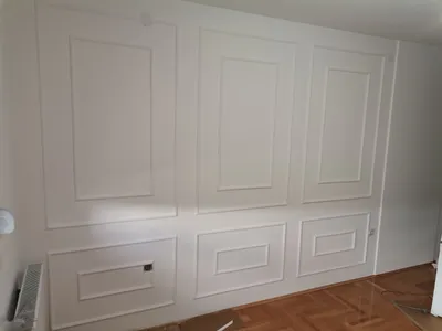 Beli zid ukrašen ramovima od stiropora: tri velika i tri mala polja iznad parketa, klasičan izgled kao gips