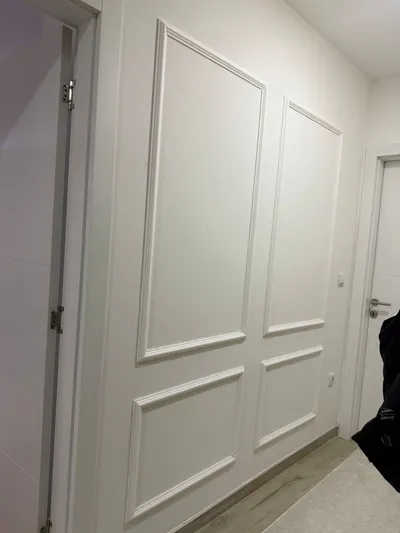 Hodnik sa belim ram lajsnama na zidu između dvoja vrata, gore visoka polja, dole niža