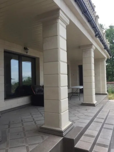 Natkrivena terasa sa četvrtastim fasadnim stubovima sa horizontalnim urezima i podom od kamenih ploča