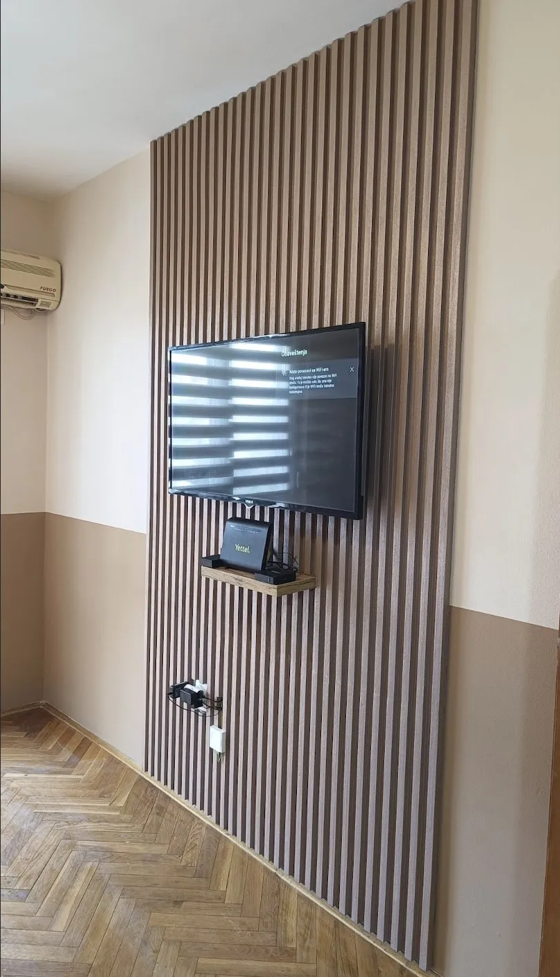 Zid sa letvicama u boji drveta od poda do plafona, televizorom na zidu, bež donjim delom zida i parketom riblja kost