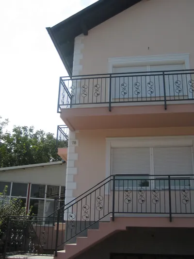 Fasada boje breskve sa dva balkona, belim okvirima oko prozora i fasadnim kockama na uglu kuće
